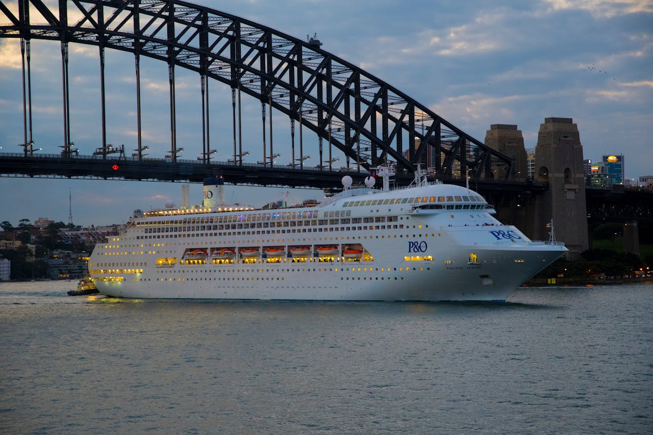 P&O cruise ship sailing beneath Sydney Harbour Bridge at dusk