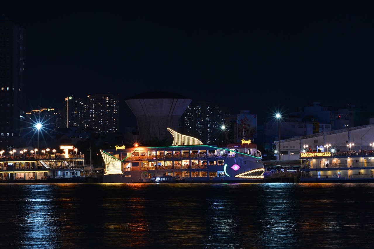 Illuminated sightseeing boats cruising through a city harbor at night
