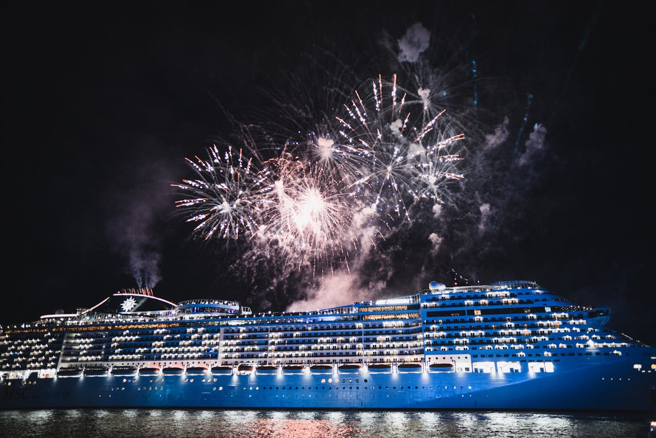 Cruise ship illuminated at night beneath a fireworks display