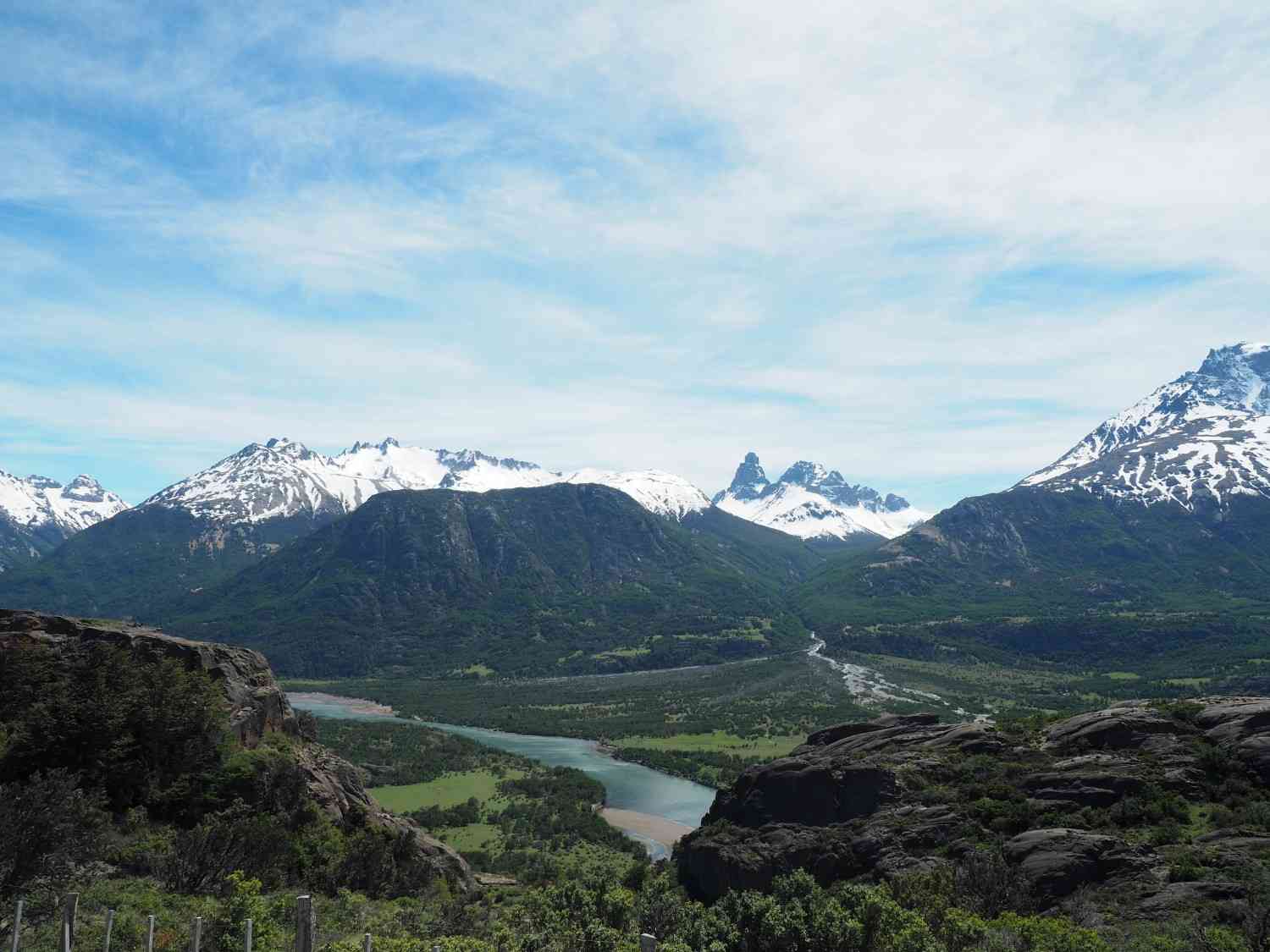 Snow-capped mountains overlooking a lush valley and winding turquoise river