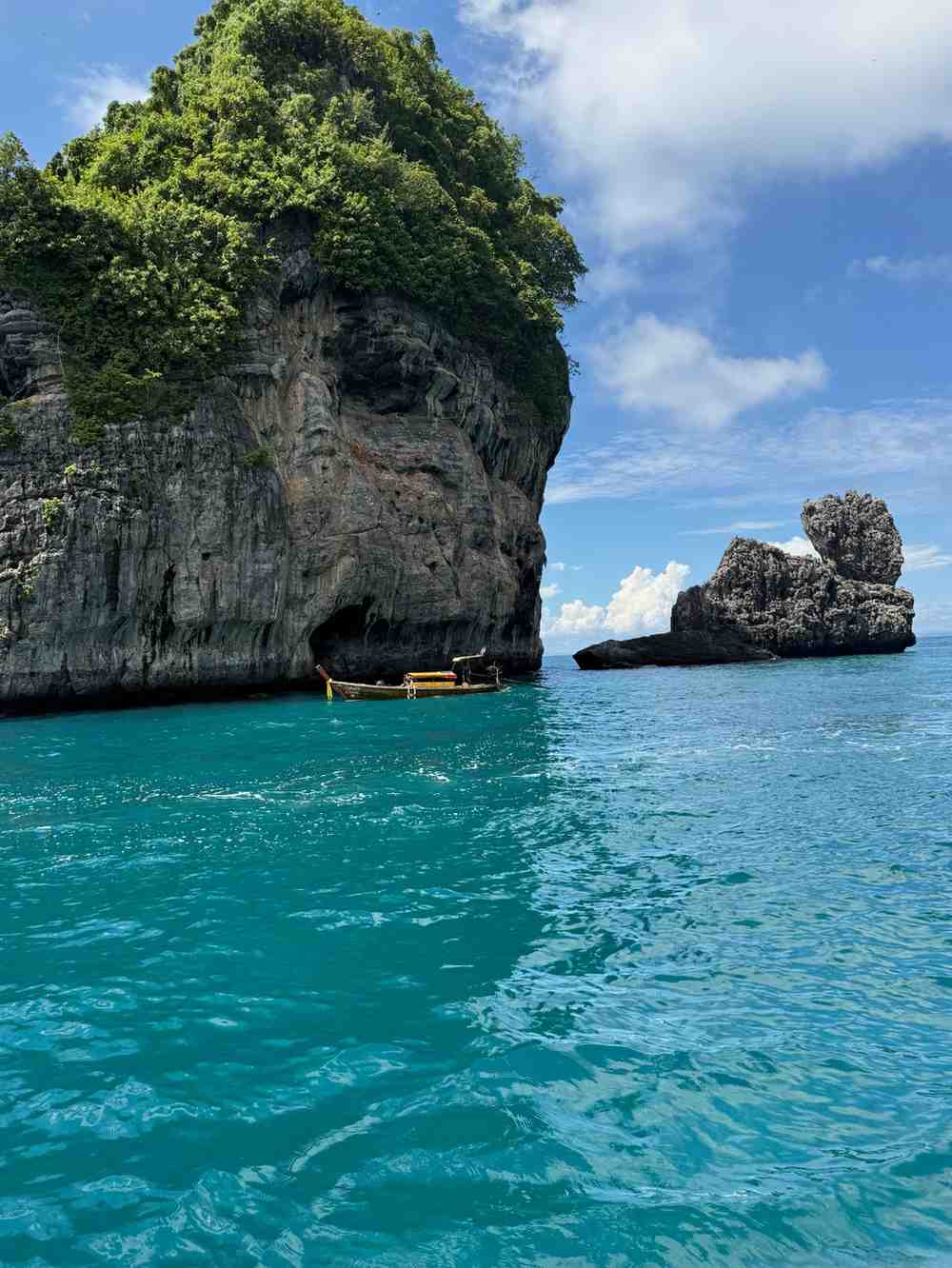 Traditional long-tail boat beside dramatic limestone cliffs in turquoise Thai waters