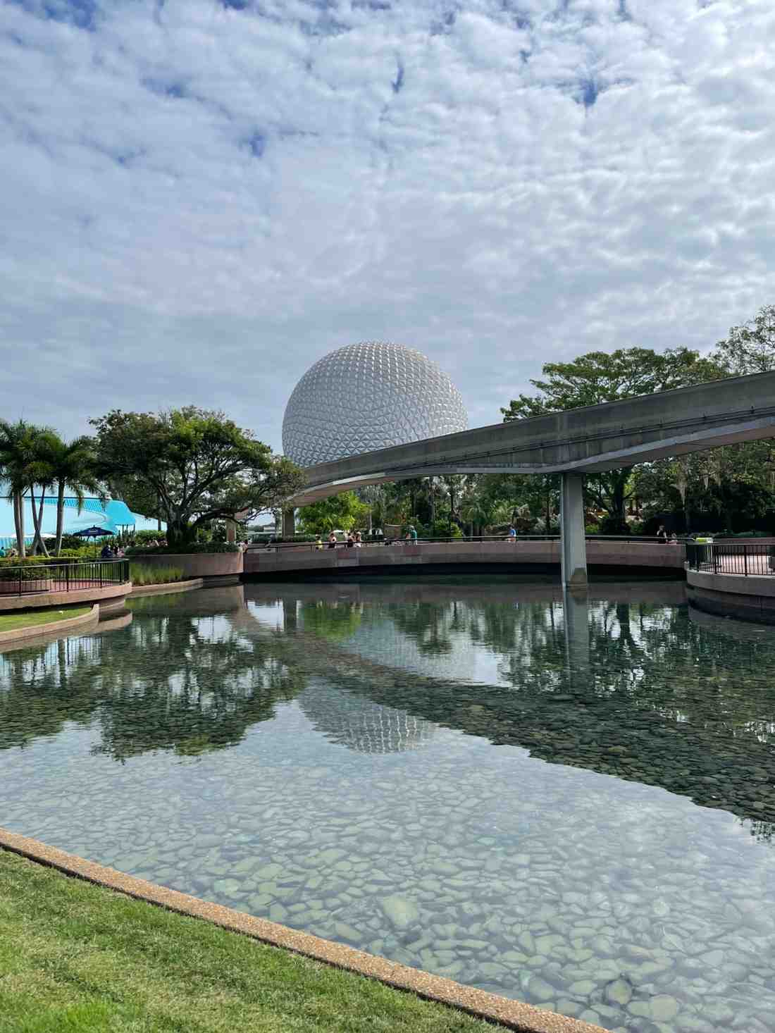 EPCOT Spaceship Earth sphere reflected in a lagoon beneath cloudy blue skies